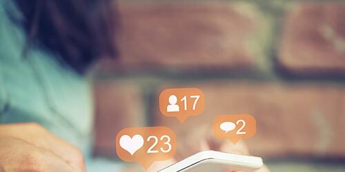 Someone using a mobile to access social media, with heart number icons floating above phone